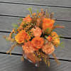 Orange roses and peach carnations in a clear square vase