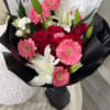Bouquet of pink gerbera daisies, red roses, and white lilies in black wrap
