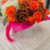 Orange roses and burgundy daisies in a white gift box with a pink ribbon.