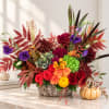 Autumn floral arrangement in a woven basket with red, purple, orange, and green blooms
