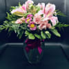 Pink lilies and roses in a glass vase with a magenta ribbon