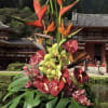 Tropical flower arrangement with orange heliconia and orchids in a white vase