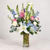 Tall mixed bouquet in a clear glass vase with lilies, roses, hydrangeas, and blue flowers