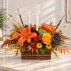Autumn floral arrangement with orange lilies, roses, and candles in a wooden box