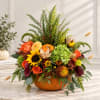 Autumn floral arrangement in a pumpkin container with orange, yellow, and green blooms