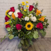 Mixed bouquet of red roses, lilies, white daisies, and a sunflower in a glass vase