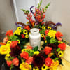 Circular floral arrangement with orange roses, yellow daisies, and a white vase in the center
