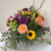 Mixed bouquet of purple, peach, and yellow flowers in a clear vase