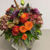 Low glass vase arrangement with bright orange and red roses, purple calla lilies, and antique hydrangeas