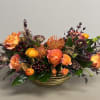 Low centerpiece of orange roses, pincushion protea, and dark berries in a striped gold bowl