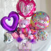 Bright pink and purple foil balloons, a cuddly pink teddy bear, and