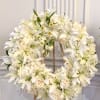 A large circular sympathy wreath arranged with serene white lilies, pale blush