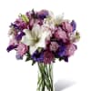 Purple and pink mixed bouquet with white lilies in a clear glass vase