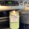 Lit green candle in a glass jar with a hanging label