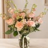 Peach roses and pink orchids in a glass vase with ribbon
