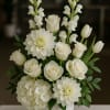 White floral arrangement in a white vase with roses, dahlias, hydrangea, and snapdragons