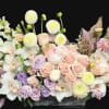 Pastel floral arrangement with roses, orchids, and round white blooms in a low container