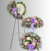 Three floral sympathy pieces with pink and white flowers and purple ribbons on stands.