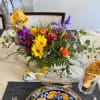 Colorful mixed flower arrangement in a clear glass vase on a dining table