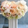 Pastel peach and white roses and ranunculus arranged in a white ceramic vase