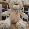 Large beige teddy bear with a plaid bow sitting on a wooden shelf