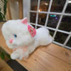 White plush cat with pink ears and a ribbon on a wooden shelf