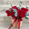 Red roses in a woven basket with a burgundy ribbon and eucalyptus