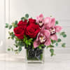 Red roses and pink orchids in a square glass vase with a black ribbon