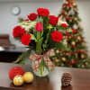 Red carnations and tulips in a glass vase with plaid bow, with ornaments and a pinecone on the table.
