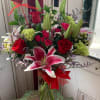 Bouquet of red roses and pink lilies in a glass vase with a heart pick