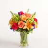 Mixed bouquet of orange lilies, roses, and colorful flowers in a clear glass vase