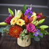 Mixed bouquet in a cream vase with purple, yellow, and orange blooms