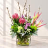 Colorful floral arrangement in a clear square vase with pink, purple, and green blooms