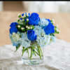 Blue roses and pale hydrangeas in a clear glass vase