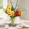 Yellow and orange orchids in a round glass vase with pebbles