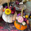Two small pumpkins topped with colorful dried flowers and moss