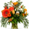 Mixed bouquet of orange, white, and yellow flowers in a clear glass vase