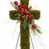 Red roses arranged on a moss-covered cross with trailing branches