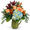 Bouquet of peach roses, blue hydrangeas, and orange mums in a green pitcher