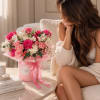 Pink and white rose bouquet in a pink hatbox beside a seated woman