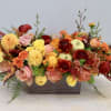 Low rectangular arrangement of orange, yellow, and red flowers with apples in a metal container