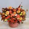 Low orange and yellow autumn flower arrangement with roses and dahlias in a terracotta pot.
