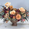 Low centerpiece of peach roses and mixed autumn flowers in a brown pedestal bowl
