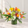 Mixed bouquet in a green glass vase with yellow, orange, white, and peach blooms