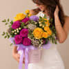 Woman holding a colorful bouquet in a pink hatbox with a ribbon
