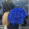 Large bouquet of vivid blue roses held in front of a shop window