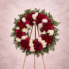 Circular floral wreath on a wooden easel with red, white, and pink flowers