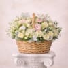 Basket arrangement of cream roses with soft pink ranunculus and white blooms on a white pedestal.
