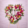 Heart-shaped standing wreath with pink and yellow roses and white daisies on a wooden easel