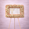 Rectangular frame of blush and cream roses around a printed cross panel on an easel.